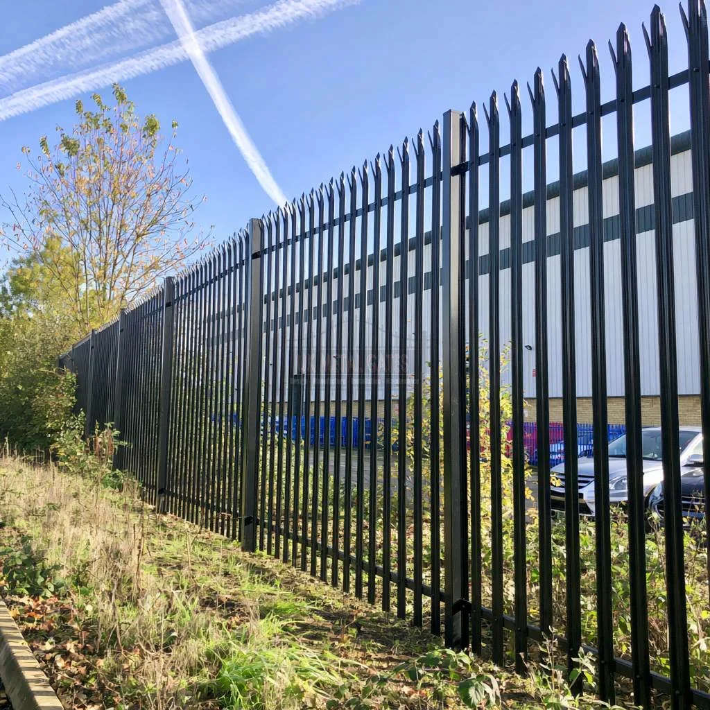 Home 90 Black palisade fencing along an industrial boundary with a tree beside it.