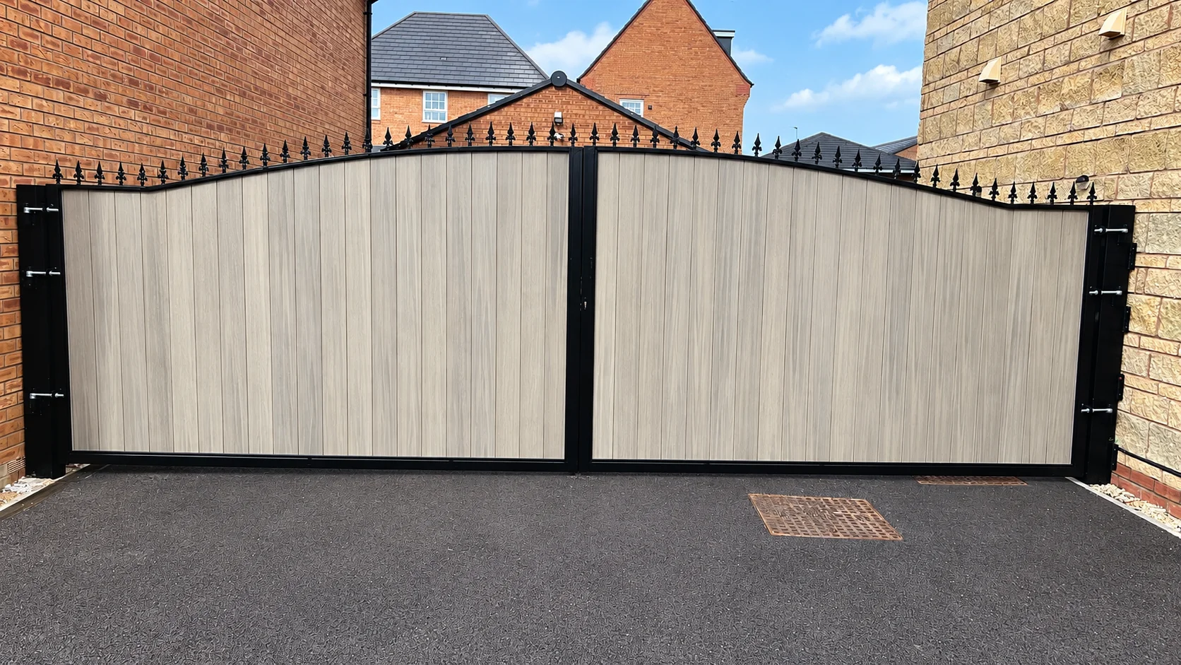 Home 44 Light grey composite driveway gates with black metal frames and spear finials between brick walls.